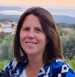 Headshot of Natalie (a woman with brown hair) with Greek countryside in the background